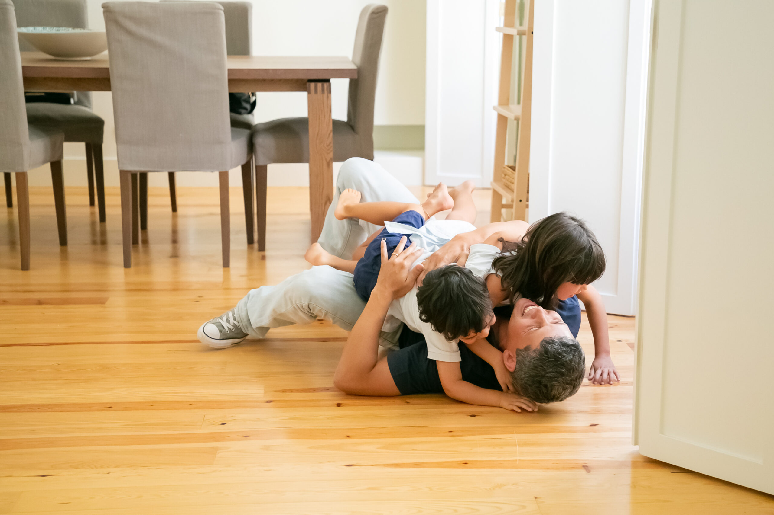 Laughing father lying on floor and hugging cute children